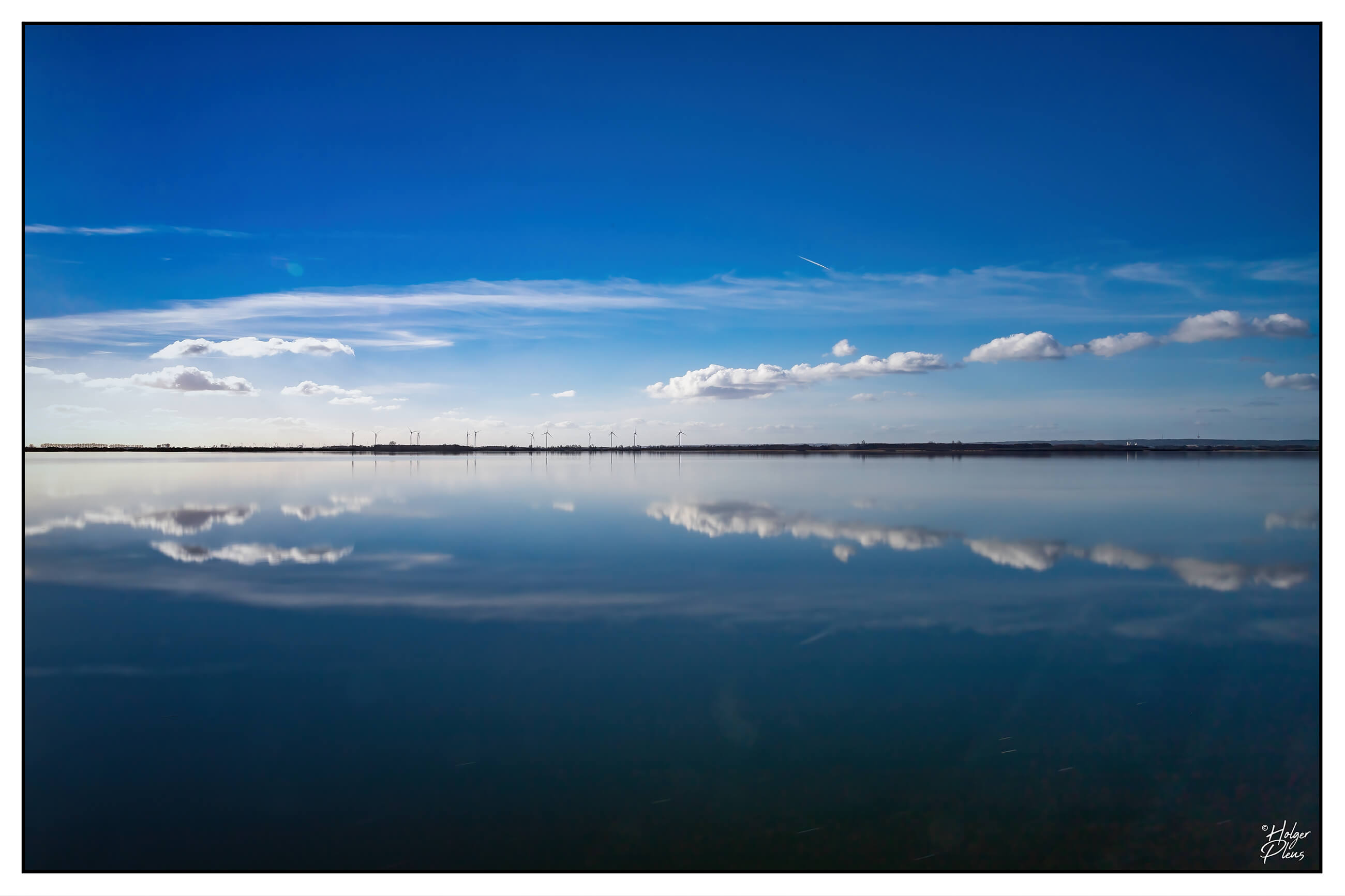 Weitwinkelaufnahme eines Sees mit Himmel darüber, nahezu monochrom blau