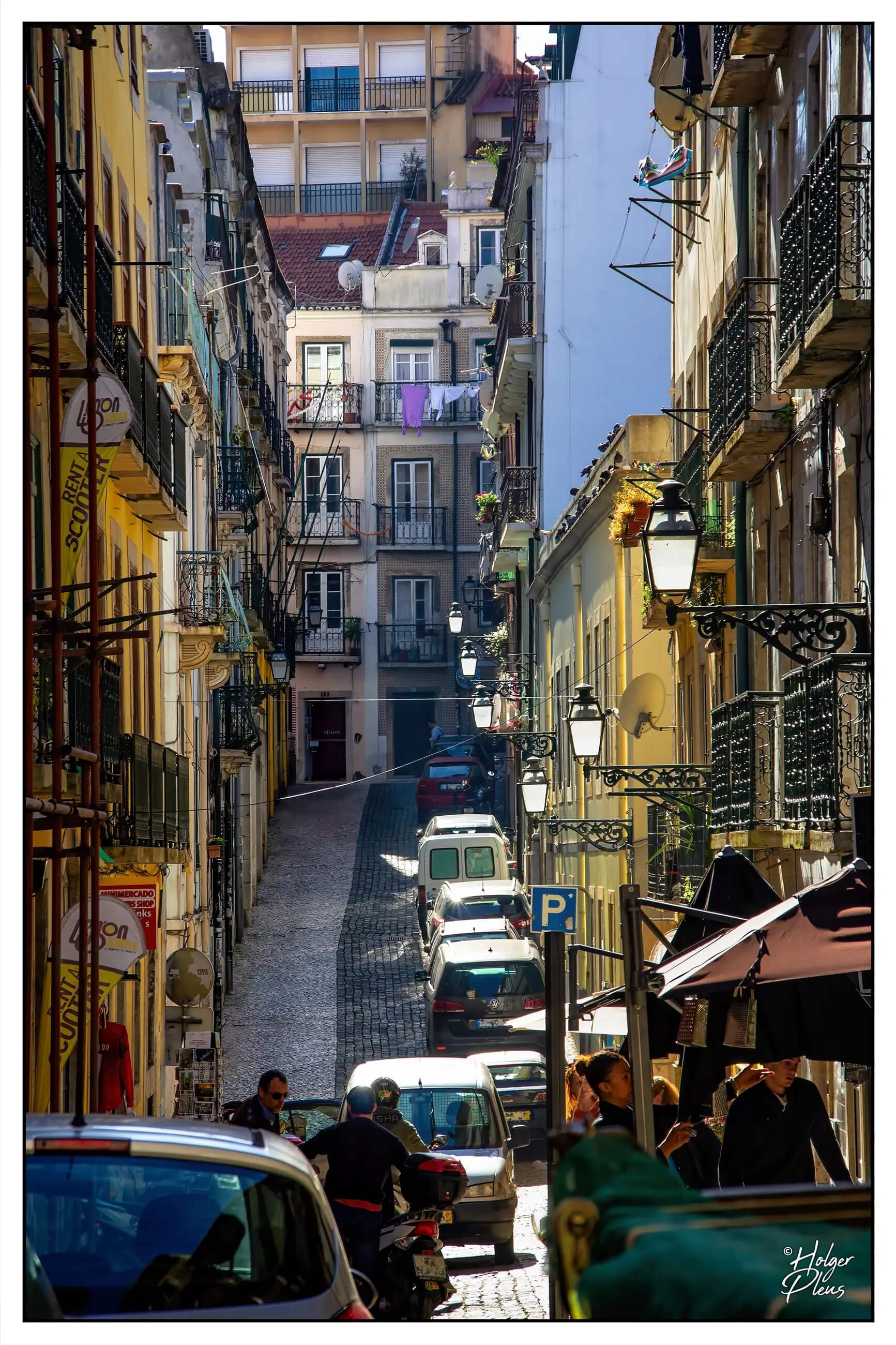 Fotografie einer schmalen Straße in Lissabon, auf der sich heitere Menschen treffen